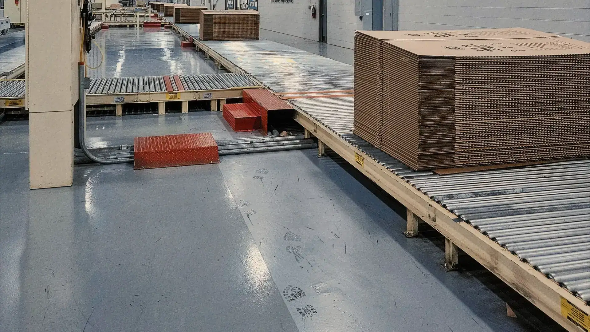 Stacks of flat corrugated board on a roller conveyor in a box factory